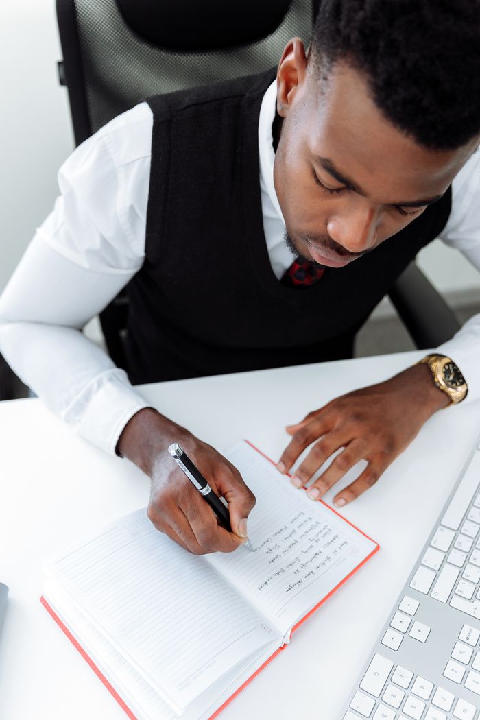 Overhead view of a focused businessman writing notes at his desk in an office setting.